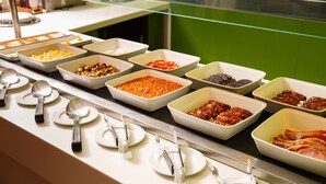 Un buffet proposant une variété de plats présentés dans des plateaux, avec des couverts et des assiettes à disposition.