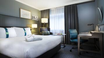Una habitación de hotel con una cama grande, un escritorio, una silla, una lámpara y una ventana con cortinas.