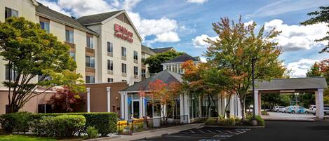 A hotel with a covered entrance, a parking lot, and a building with a sign.