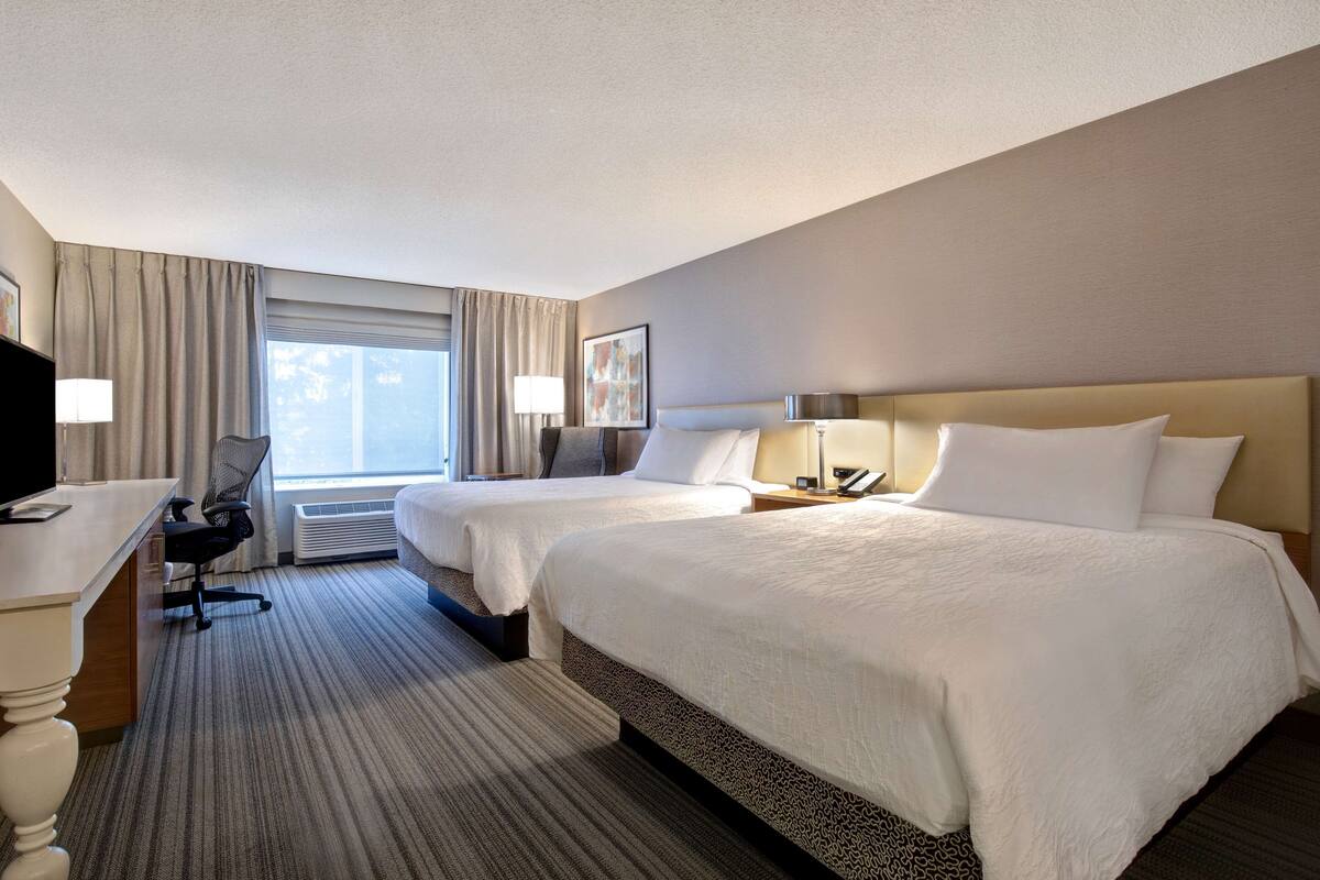 A hotel room with two beds, a desk, and a chair.