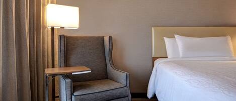 A hotel room with a bed, a chair, a small table, and a lamp.