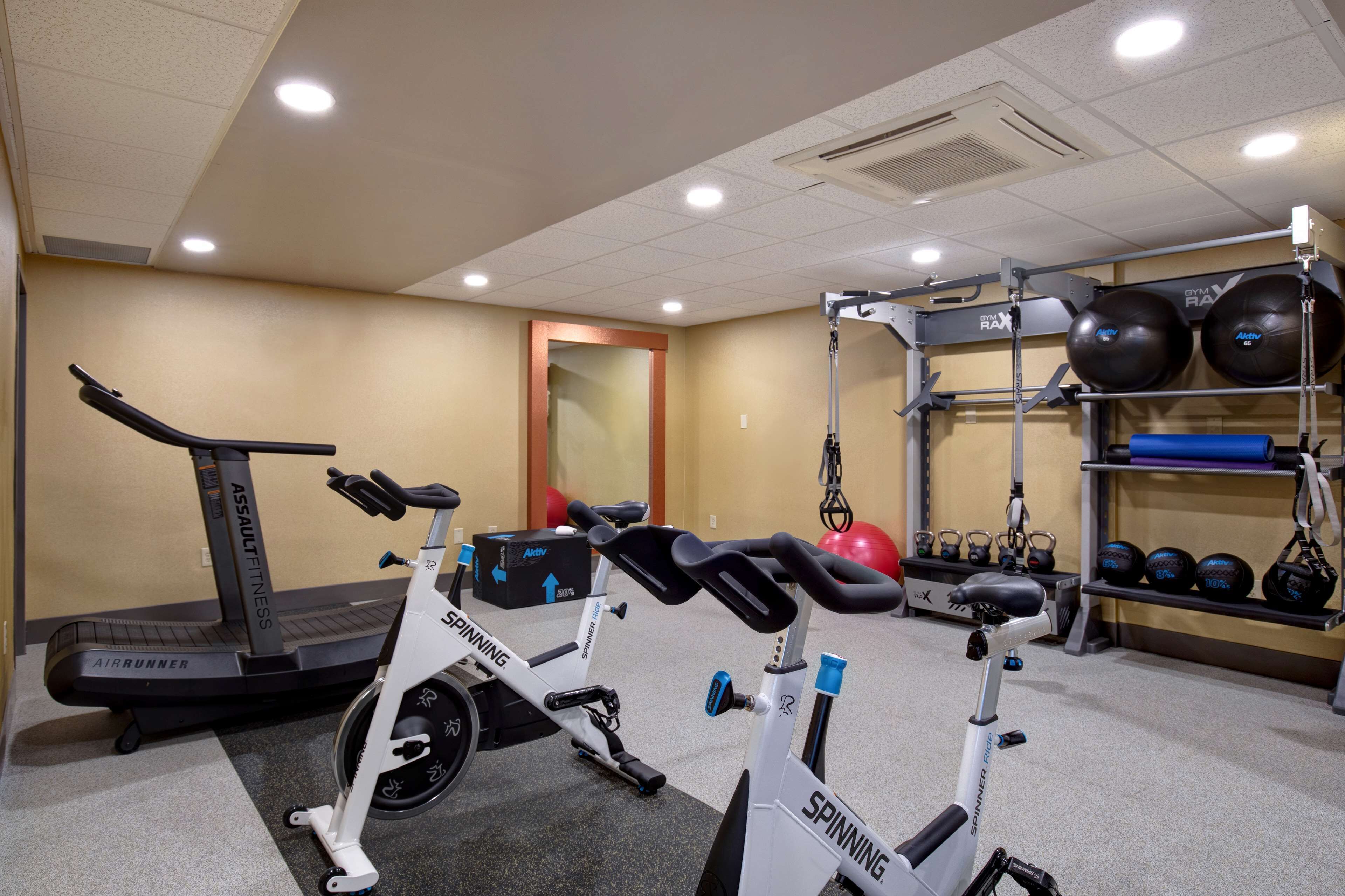 Un gimnasio con una cinta de correr AirRunner, una bicicleta spinning y un rack de pesas con pelotas de ejercicio.