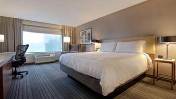 Habitación de hotel con una cama grande, un escritorio con silla, una lámpara de pie y una ventana con cortinas.