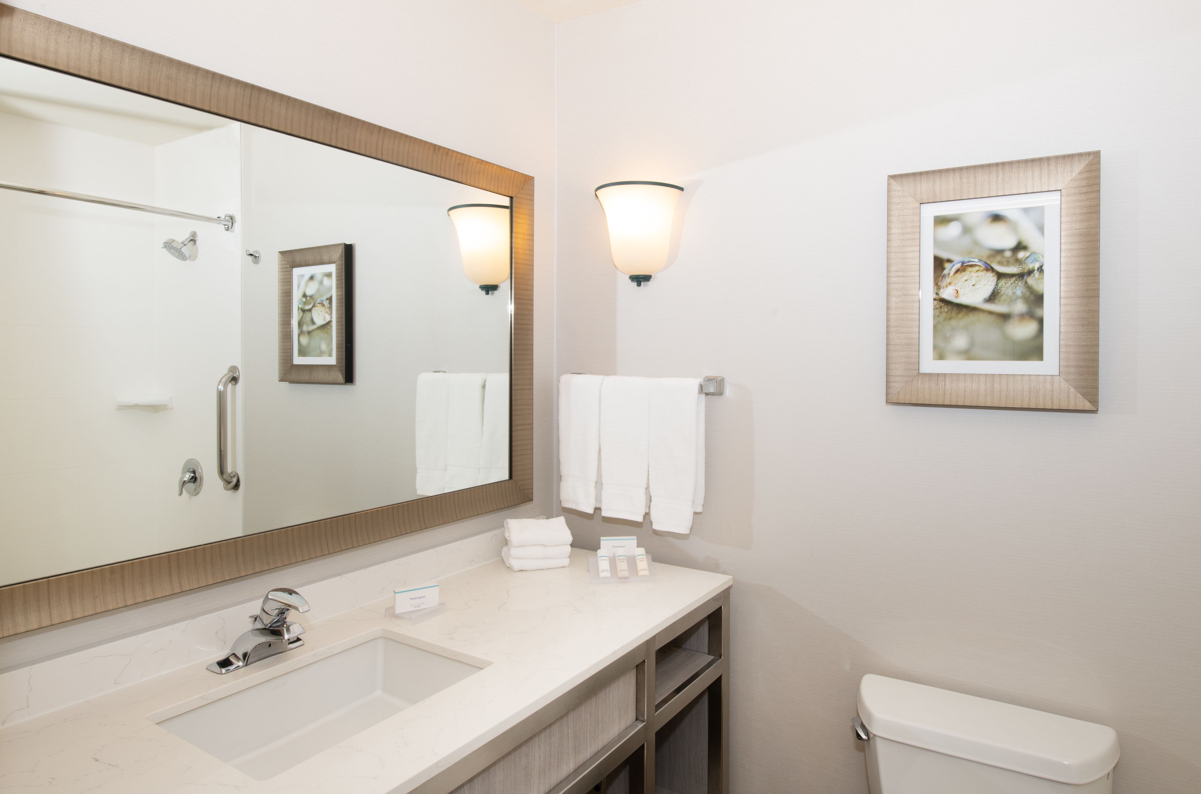 A bathroom with a large mirror, a sink, a toilet, and two wall-mounted light fixtures.