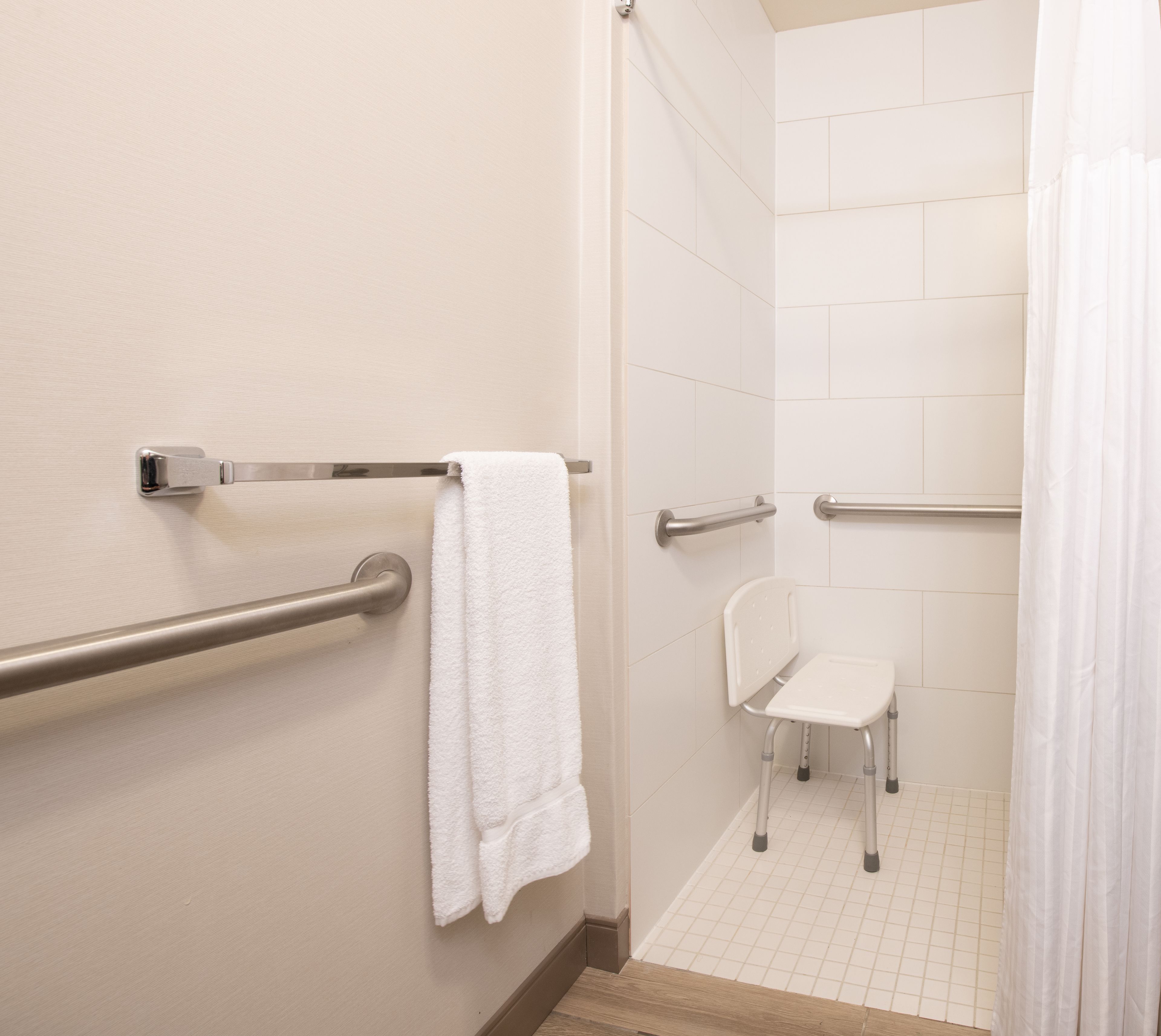 A bathroom with a white tiled floor, a white sink, a white chair, and a white towel hanging on a metal grab bar.