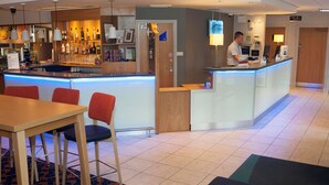 A hotel lobby with a bar area, seating, and a reception desk.