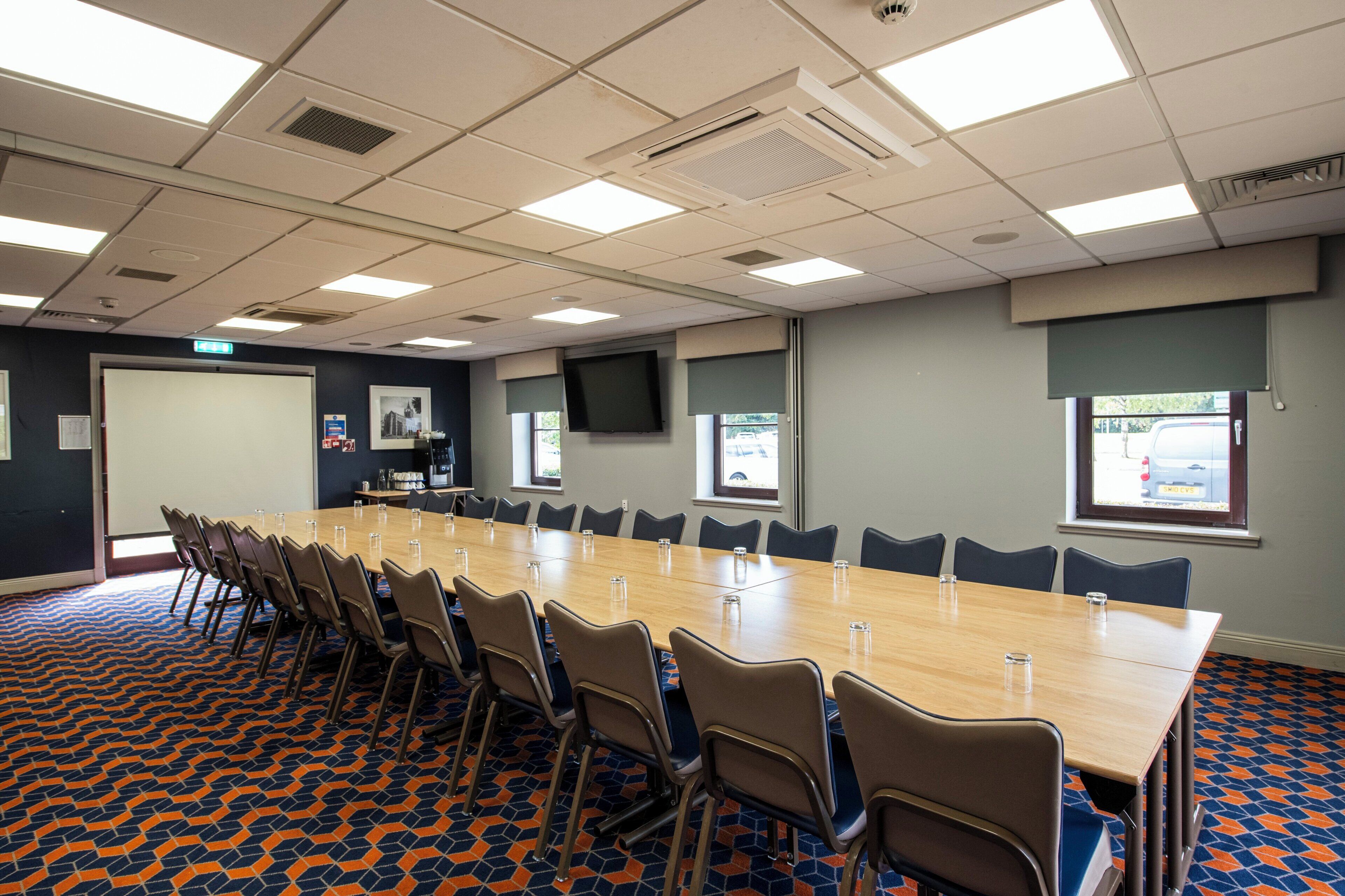 A conference room with a long table, chairs, and a projector screen.