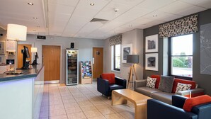 A modern hotel lobby with a reception area, seating, and a vending machine.