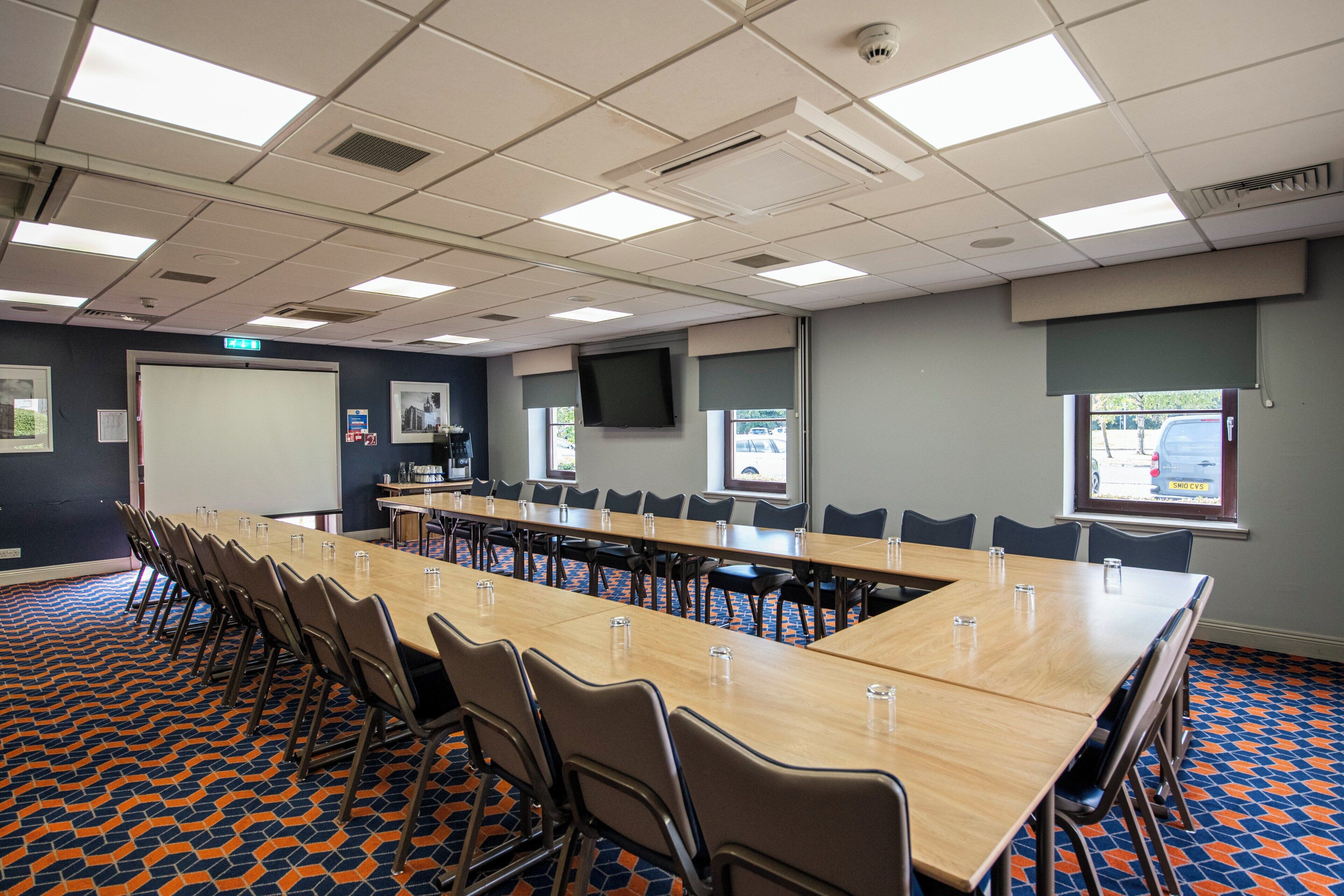 A conference room with a long table, chairs, a projector screen, and a large window.