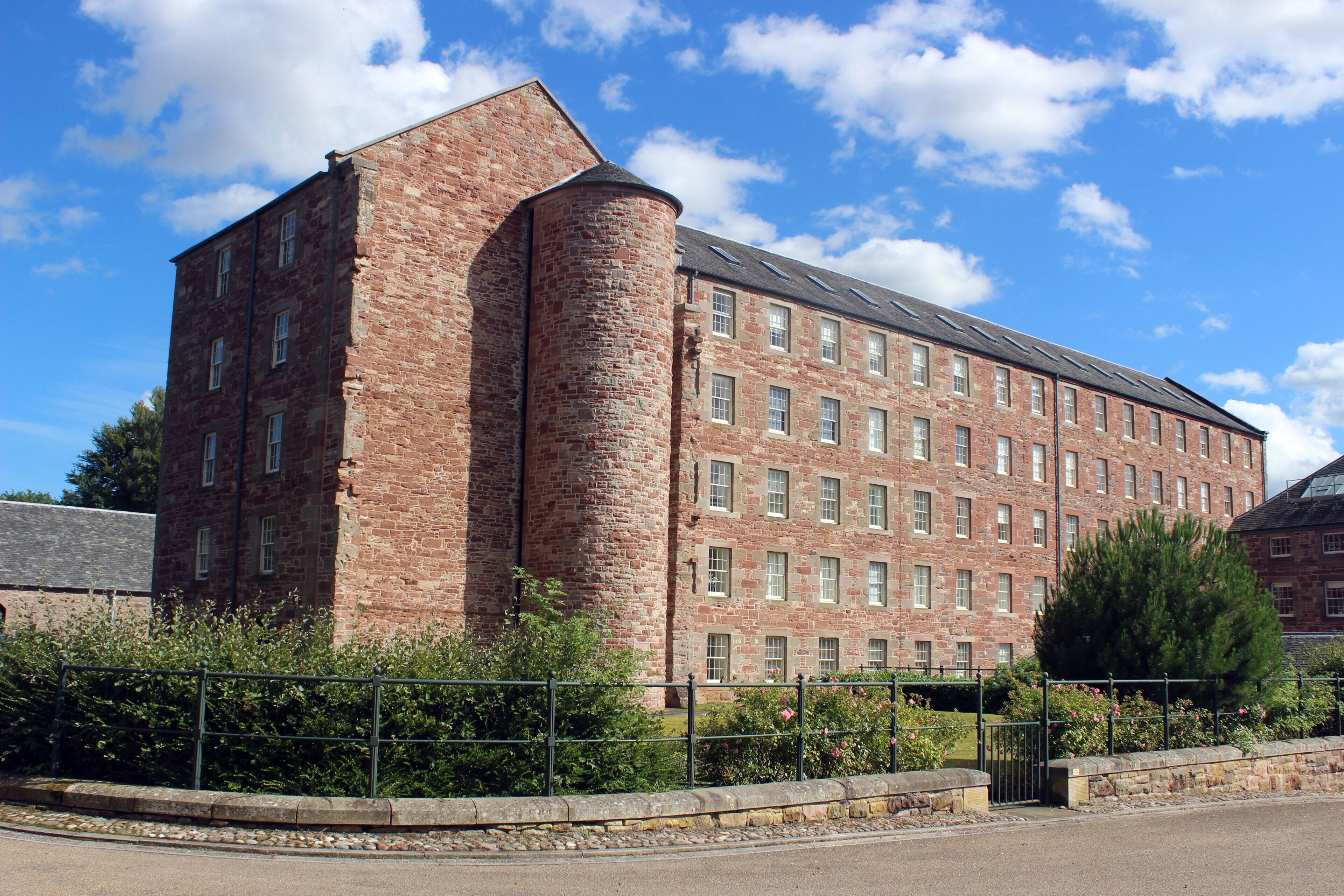 A multi-story brick building with a prominent corner tower, large windows, and a flat roof.