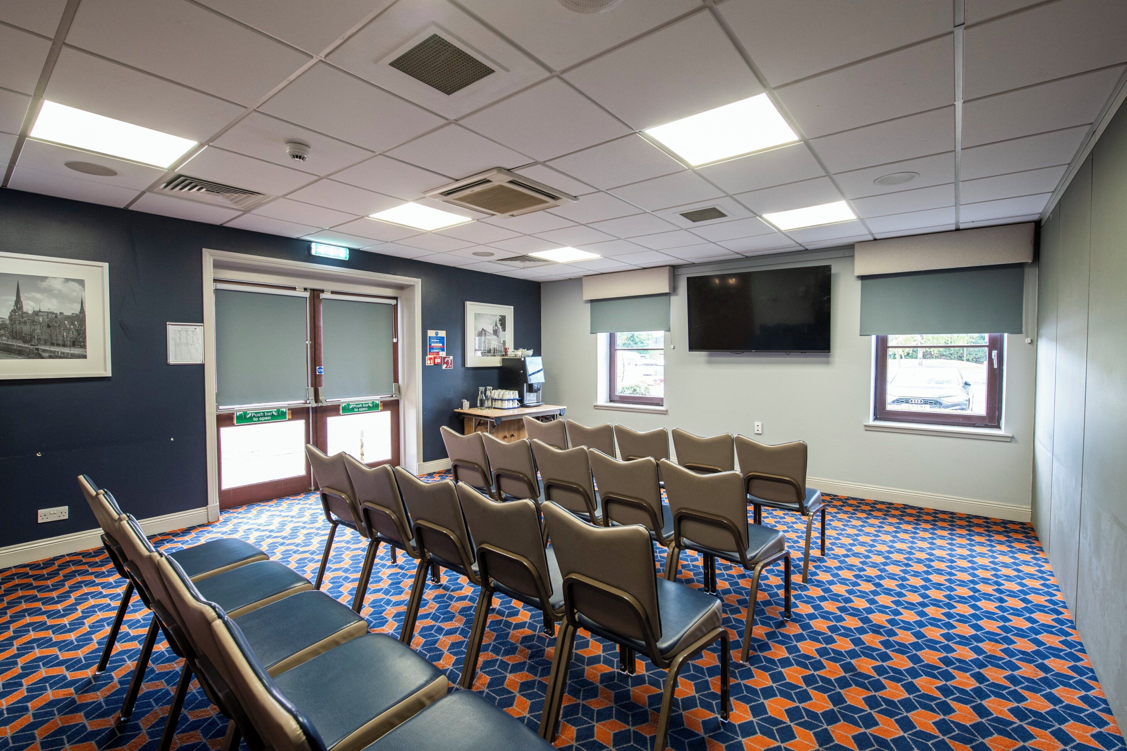 A conference room with a patterned floor, multiple chairs, a projector screen, and a door leading outside.