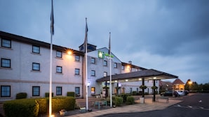 A hotel with a sign reading "Hotel Inn Express," a covered parking area, and a row of flags. - Holiday Inn Express Perth by IHG (Perth)