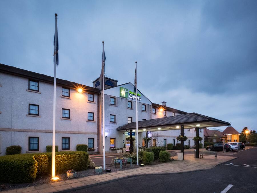 A hotel with a sign reading "Hotel Inn Express," a covered parking area, and a row of flags.