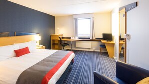 A hotel room with a bed, desk, chair, and a large mirror.