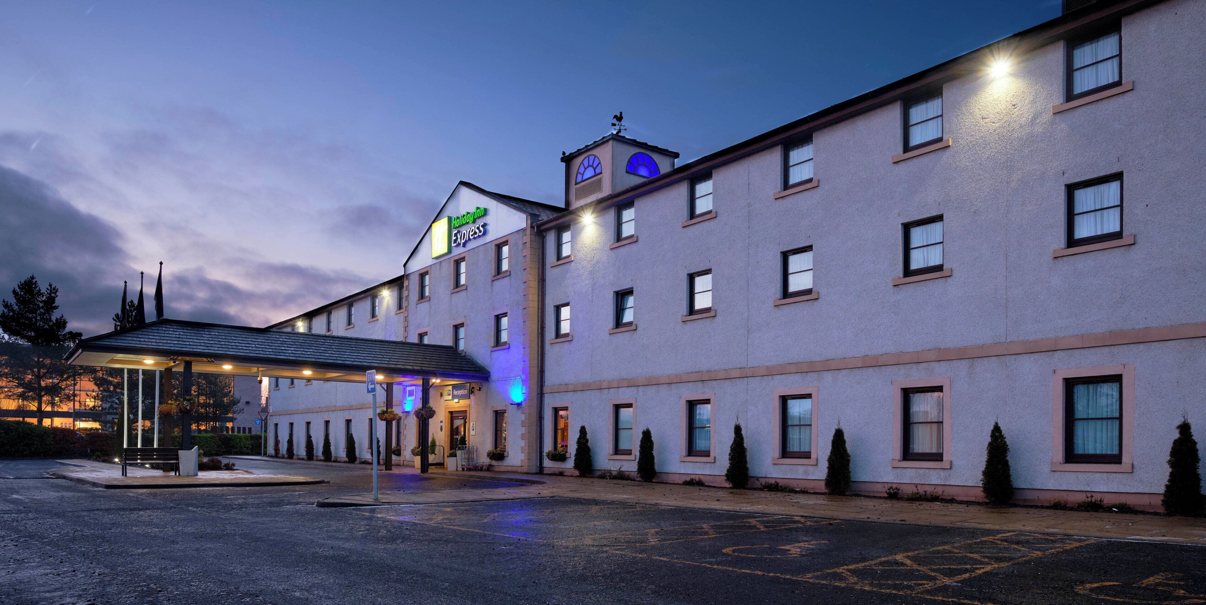 Edificio de Holiday Inn Express con acceso cubierto, varias ventanas y un estacionamiento.