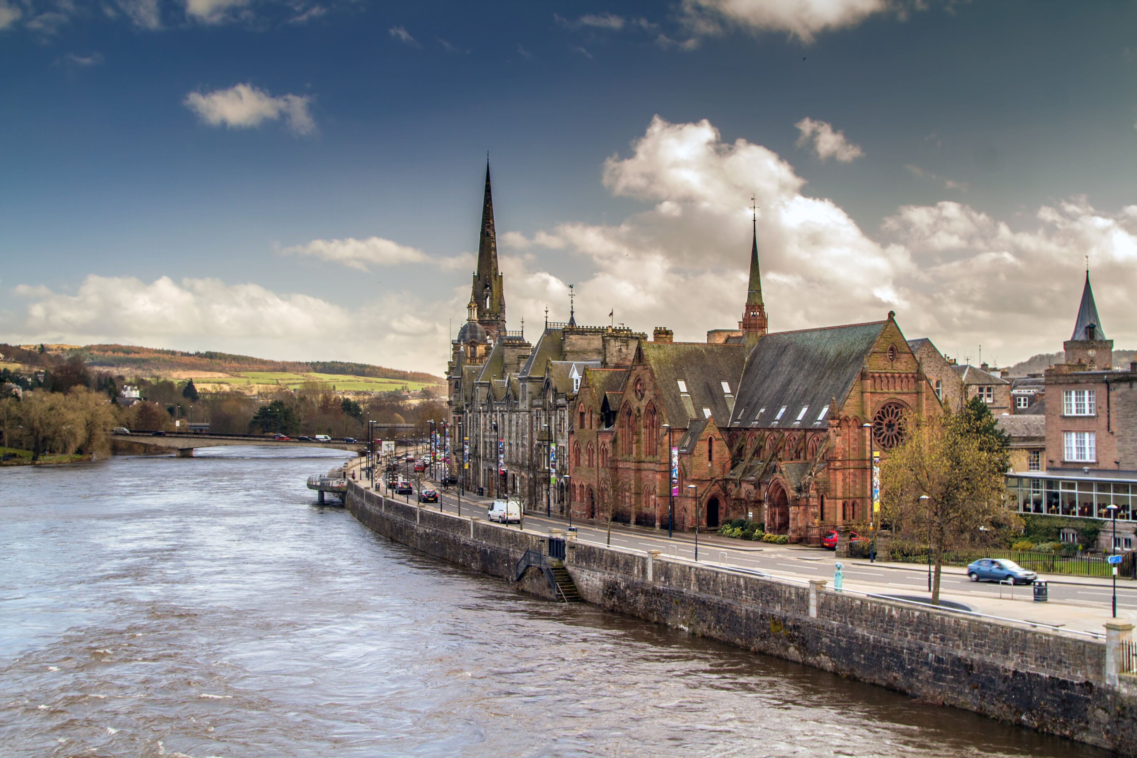 A historic building with a prominent tower, a river in the foreground, and a bridge in the background.