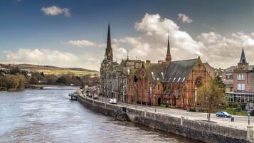 A historic building with a prominent tower, a river in the foreground, and a bridge in the background.