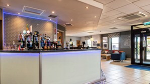 Zona de bar con mostrador, diversas botellas y un área de estar con sofá y sillones.