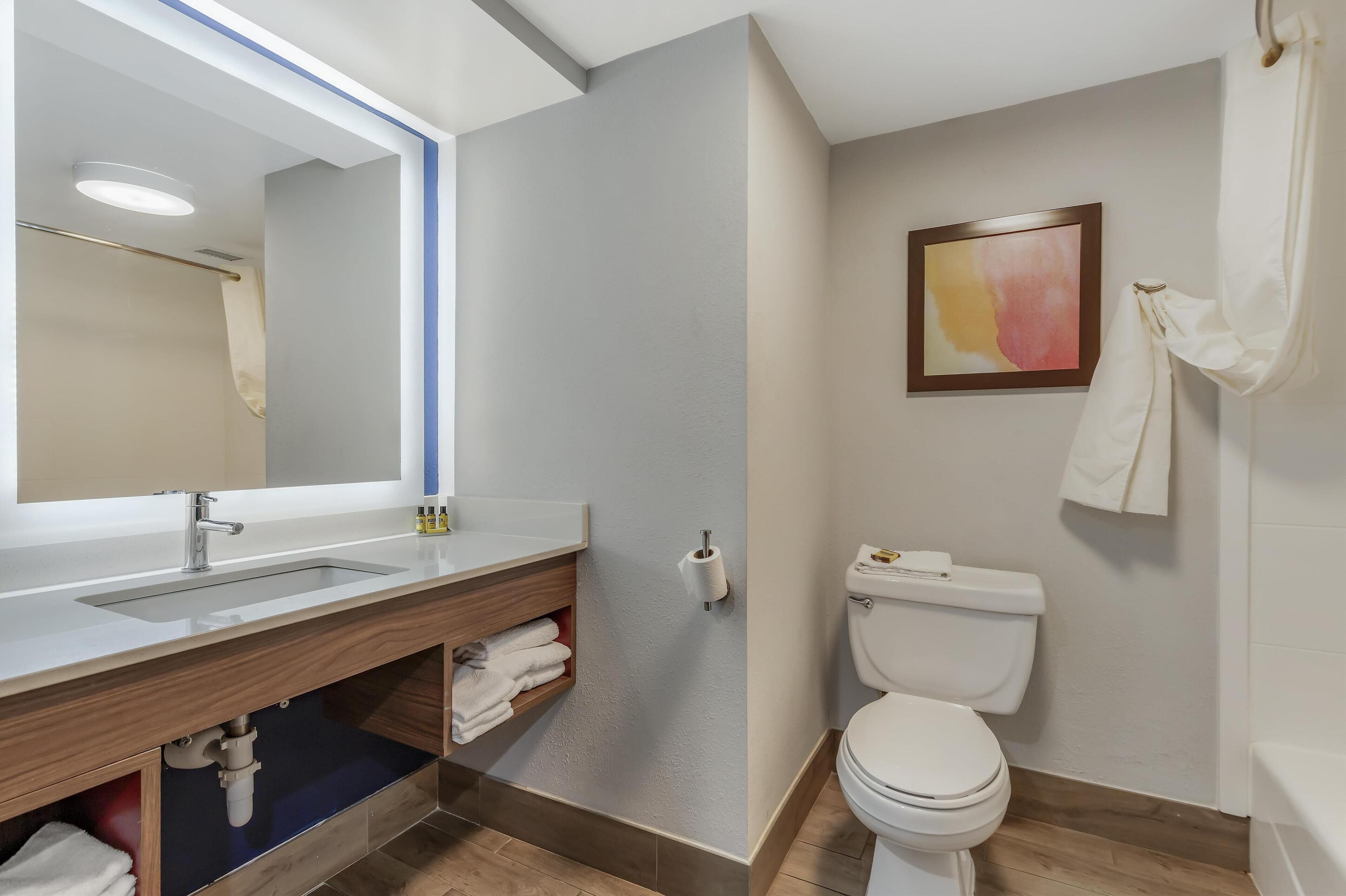 A modern bathroom with a large mirror, a sink, a toilet, and a shower area.