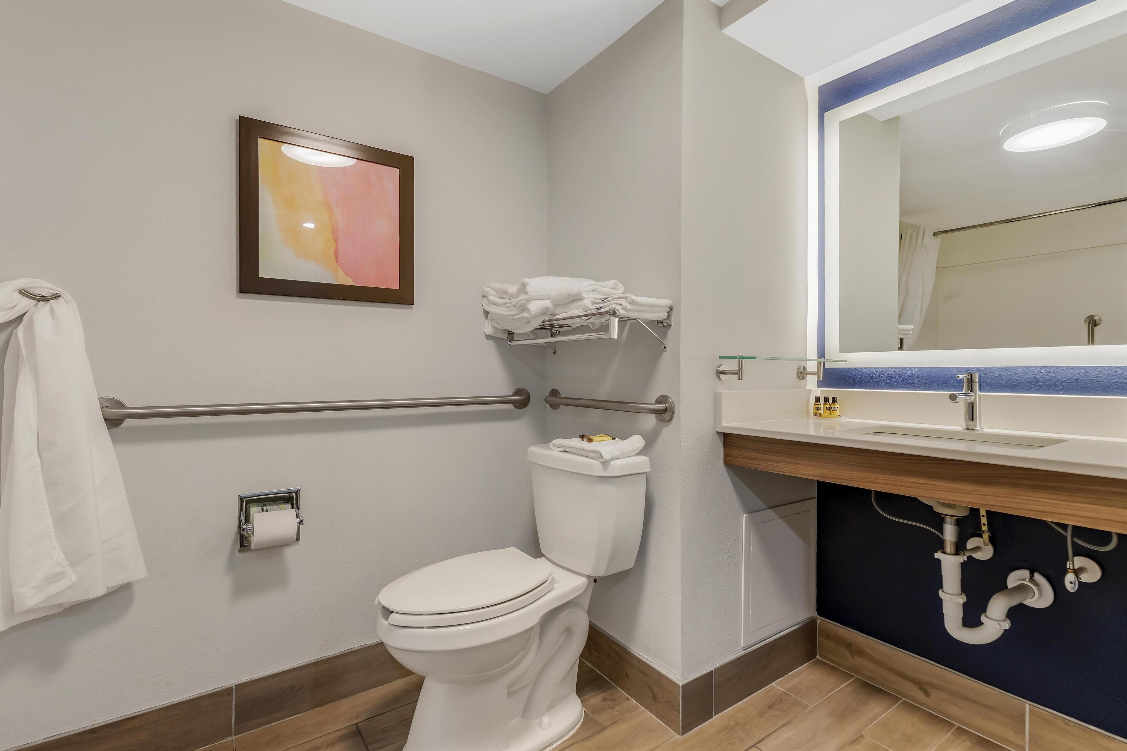 Un bagno moderno dotato di toilette, maniglioni, asciugamano e lavandino con specchio.