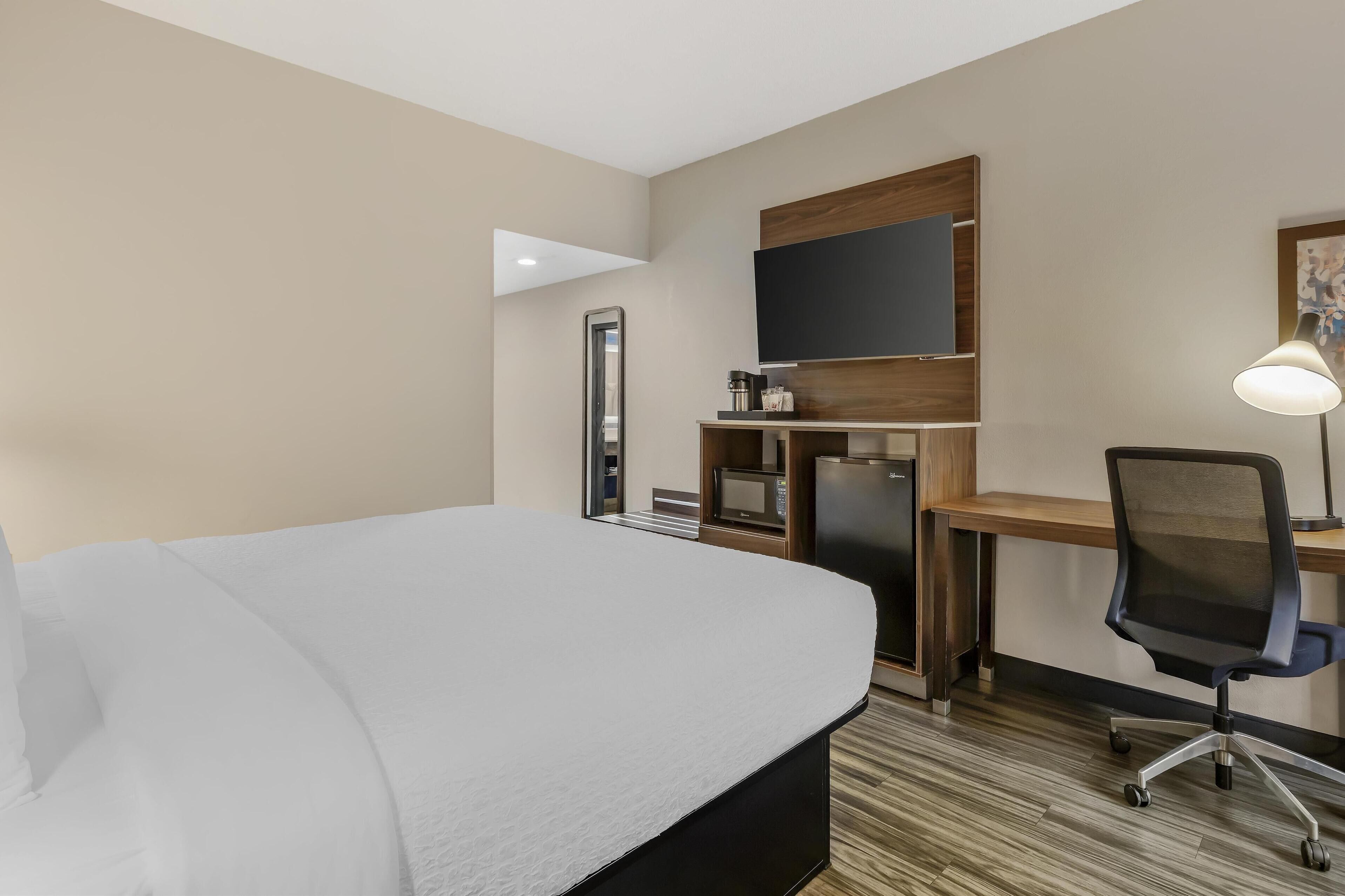 Habitación de hotel con cama, escritorio, silla, televisor y lámpara.