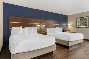 Habitación de hotel con dos camas, cabecero de madera, lámparas de noche y un cuadro en la pared.