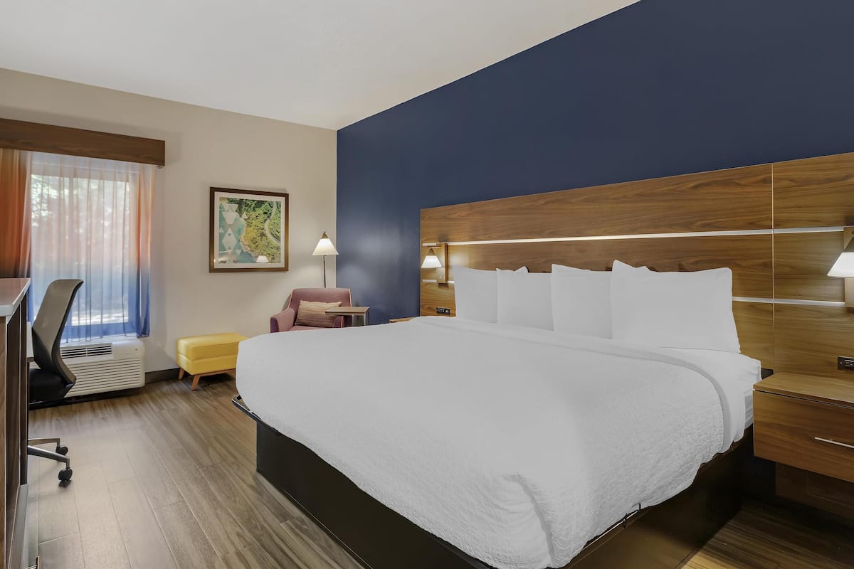 A hotel room with a large bed, a desk, a chair, a small table, and a window with curtains.