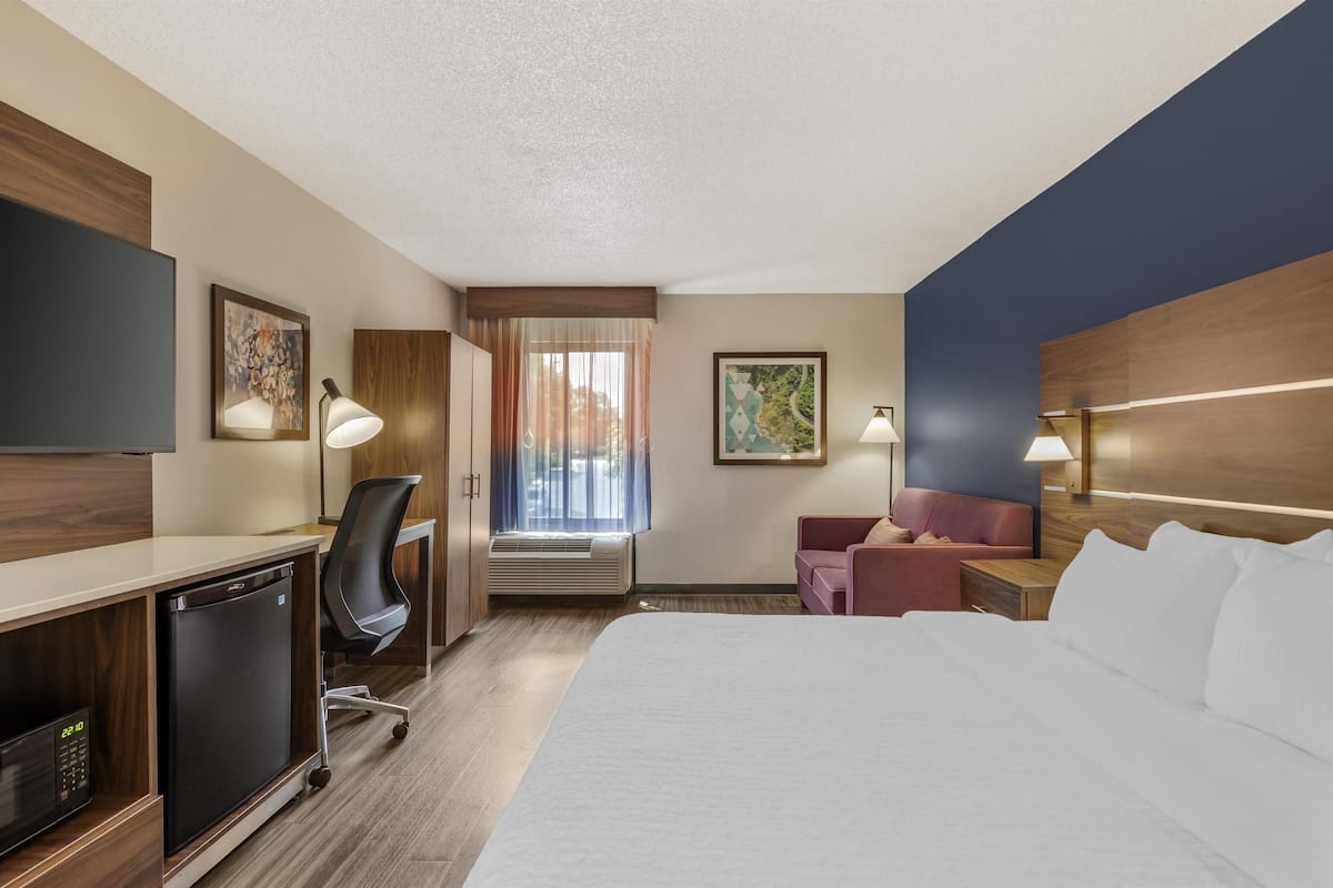 A hotel room with a bed, desk, chair, and a television.