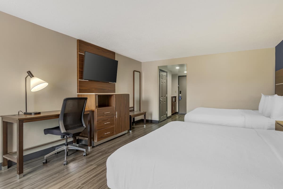 A hotel room with a bed, a desk, a chair, a TV, a wardrobe, and a mirror.