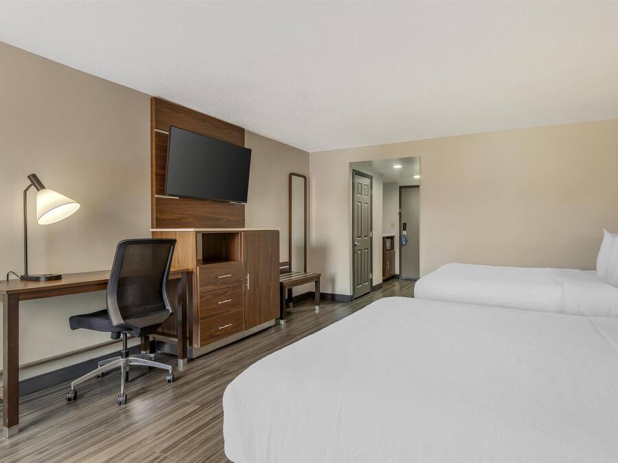 Ein Hotelzimmer mit Bett, Schreibtisch, Stuhl, Fernseher, Kleiderschrank und Spiegel.