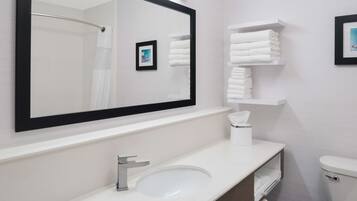 A modern bathroom with a large mirror, white sink, and towel storage.