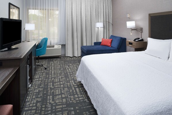 Quarto de hotel com uma cama grande, uma escrivaninha com computador, uma cadeira, um abajur e uma mesa de cabeceira com telefone.