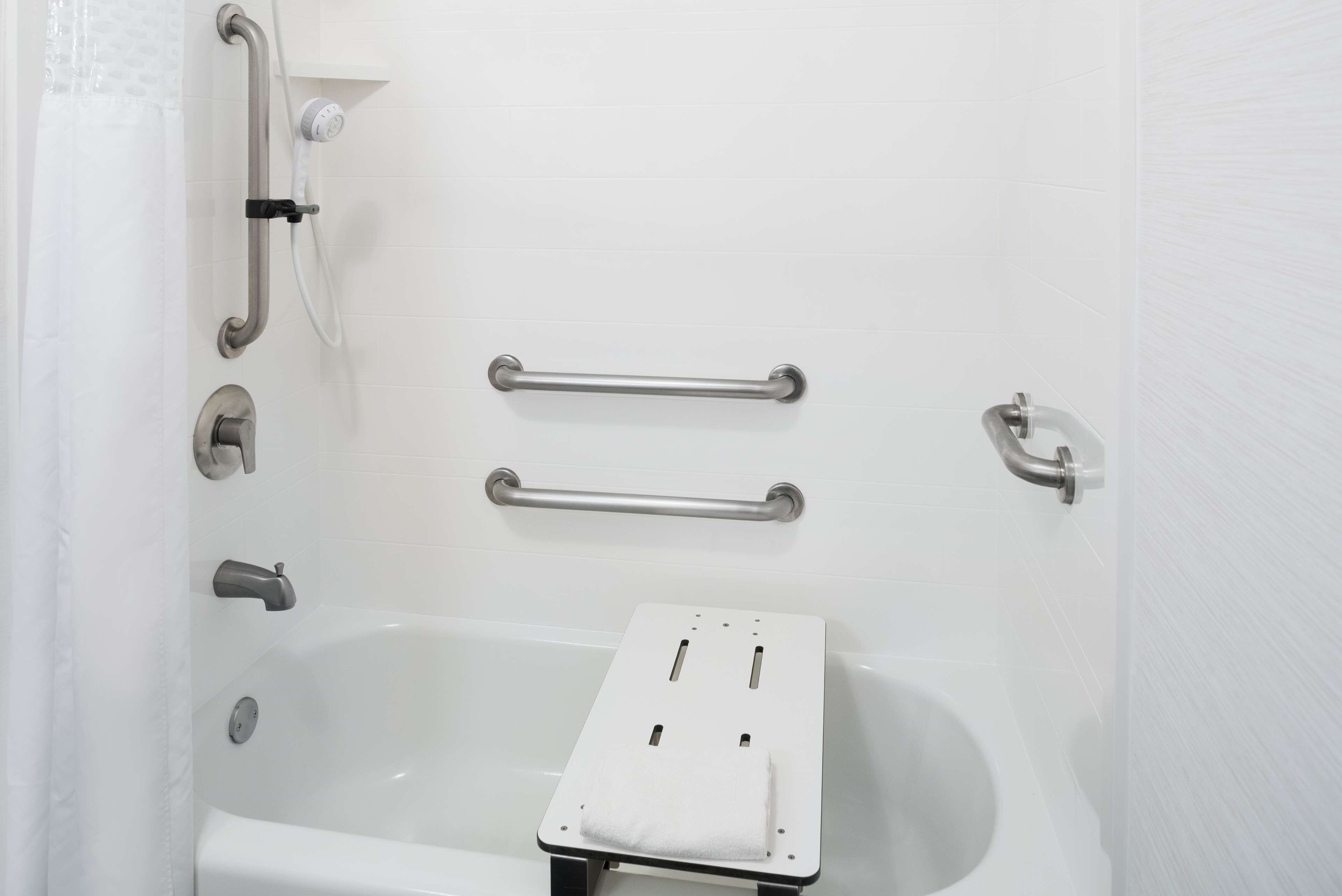 Un baño con bañera, barras de apoyo y un perchero para toallas.