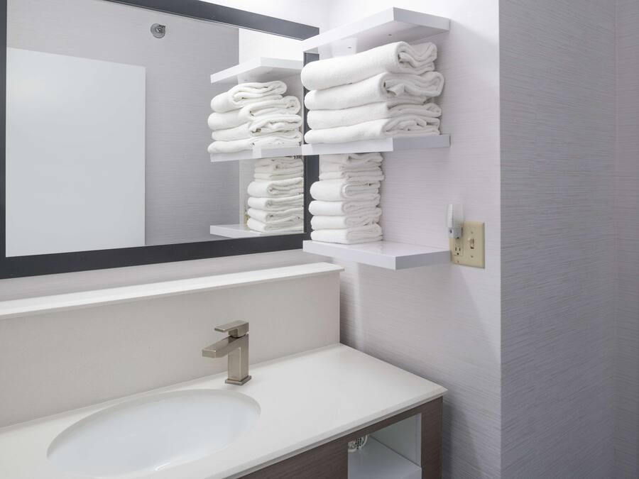 Un baño moderno con un lavamanos blanco, un espejo grande y dos toalleros con toallas dobladas con cuidado.