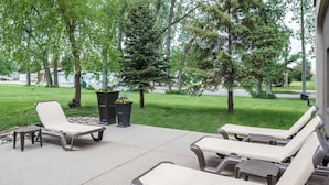 An outdoor patio with lounge chairs and a small table, surrounded by trees and a grassy area. - Hampton Inn North Sioux City (North Sioux City)