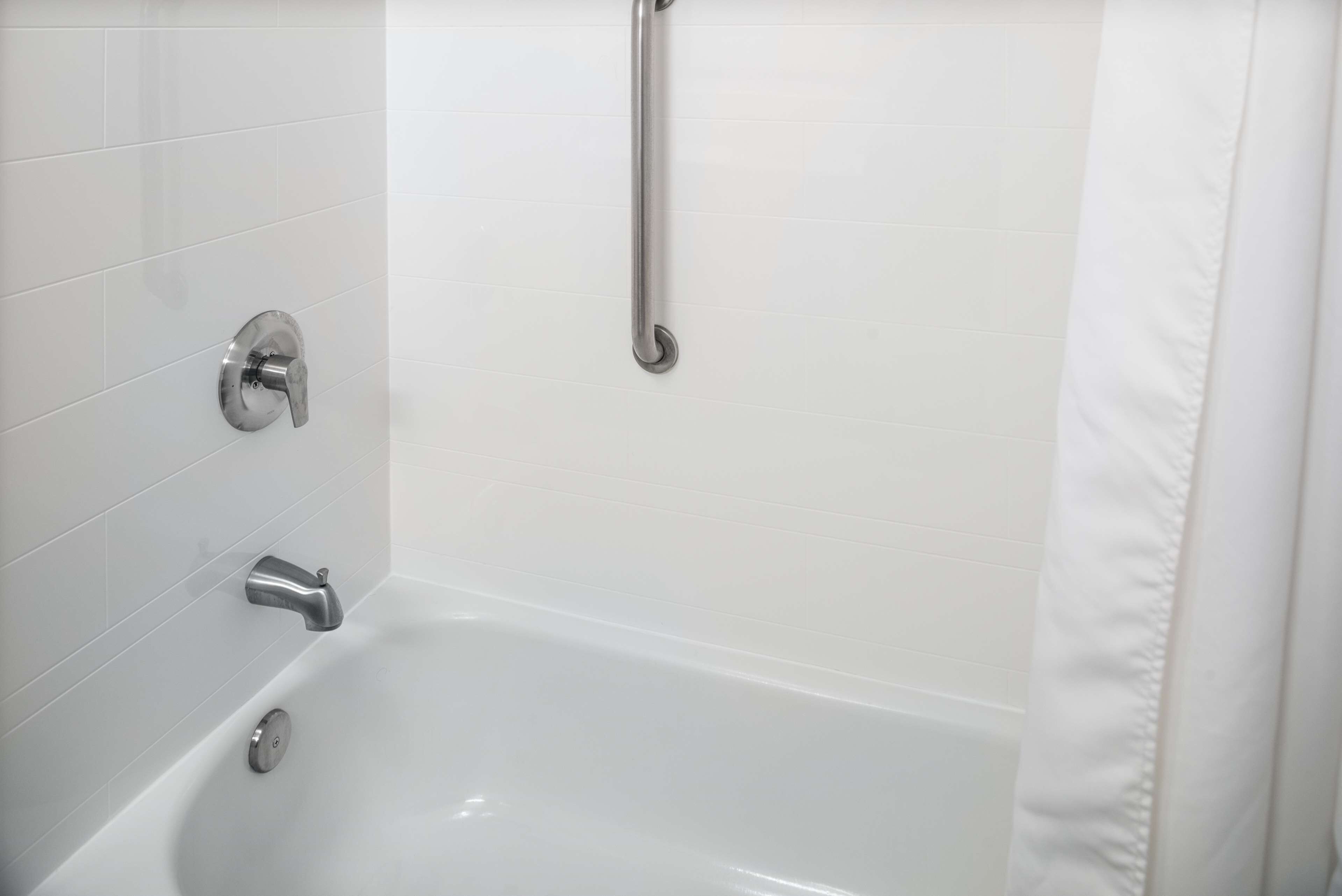 A modern bathroom with a white bathtub, a handheld showerhead, and a wall-mounted faucet.