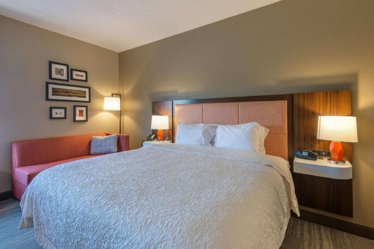 A hotel room with a large bed, a red sofa, two bedside tables with lamps, and framed pictures on the wall.