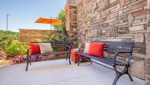 An outdoor seating area with two benches, a stone wall, and an orange umbrella. - Hampton Inn Wilkesboro (Wilkesboro)