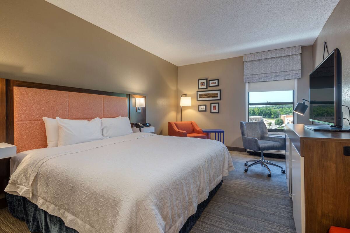 A hotel room with a large bed, a desk with a computer, a chair, and a TV.