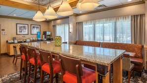 A hotel lobby with a large granite counter, multiple bar stools, a seating area with a bench, and pendant lighting. - Hampton Inn Wilkesboro (Wilkesboro)