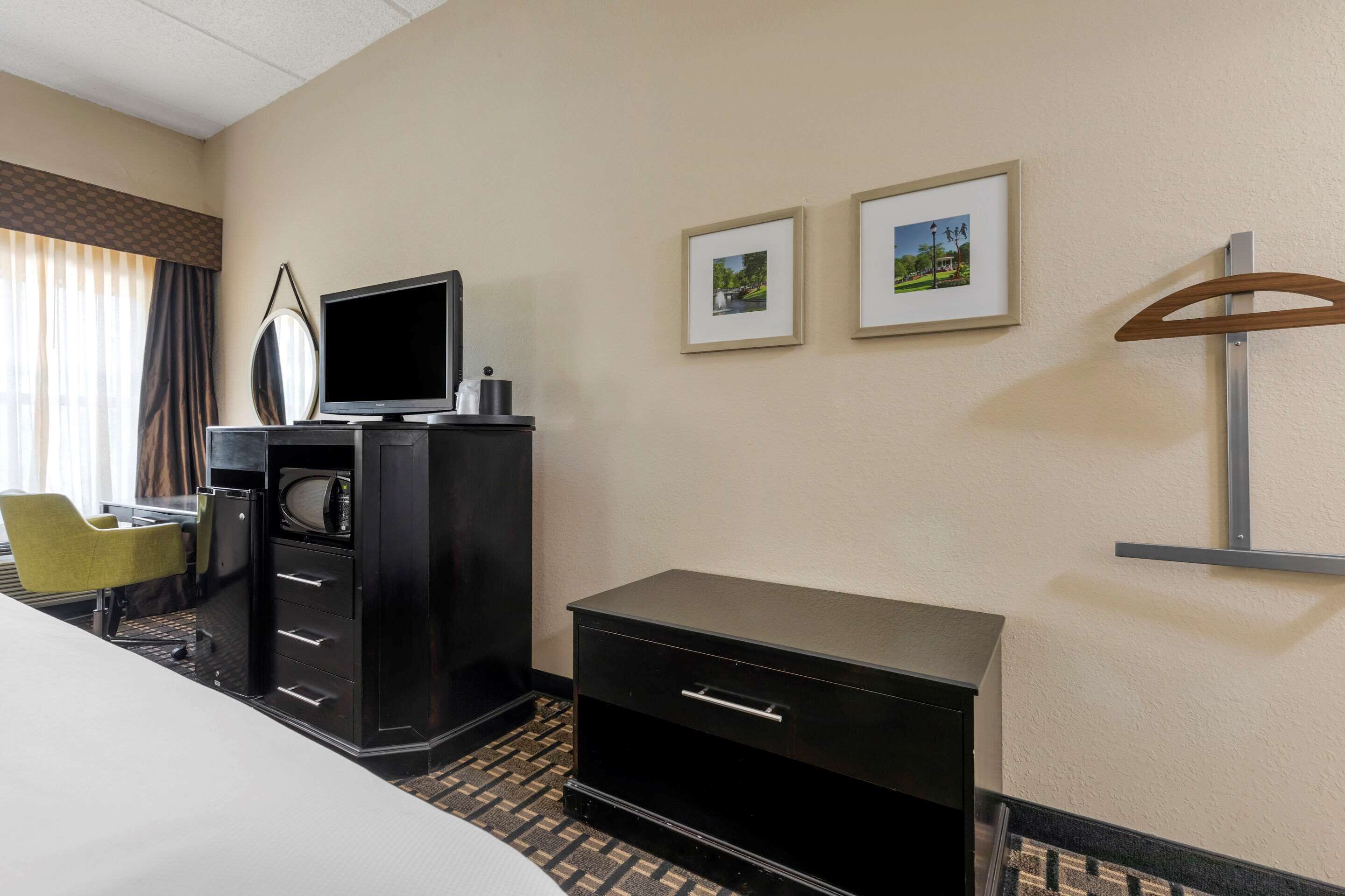 A hotel room with a bed, a desk with a computer, a TV, and two framed pictures on the wall.