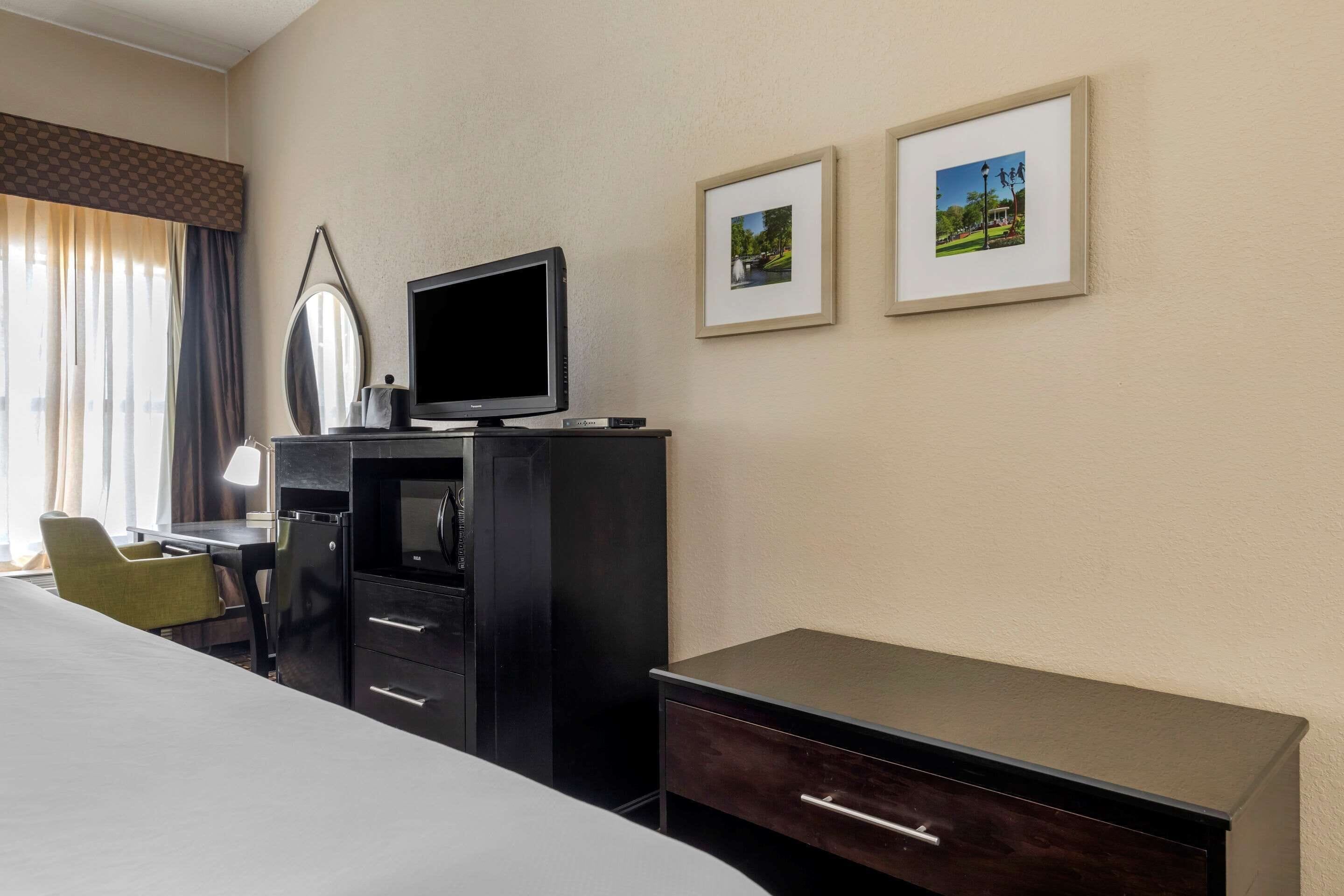 A hotel room with a bed, a desk with a computer, a TV, and two framed pictures on the wall.