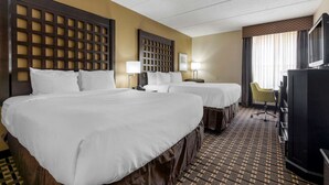 A hotel room with two beds, a desk, a television, and a chair.