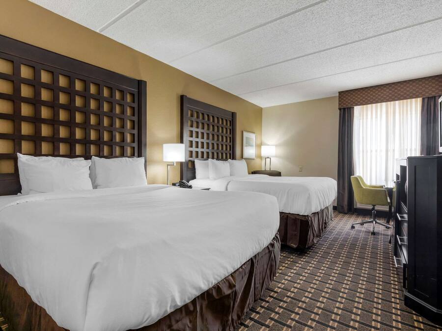 A hotel room with two beds, a desk, a television, and a chair.