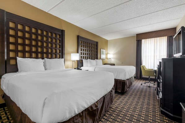 A hotel room with two beds, a desk, a television, and a chair.