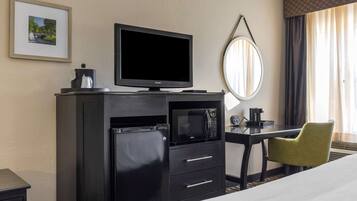 Una habitación de hotel con cama, escritorio con silla, televisión, microondas, cafetera y un cuadro en la pared.