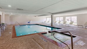 An indoor swimming pool with a clear water surface, a diving board, and a sunlit area with lounge chairs.