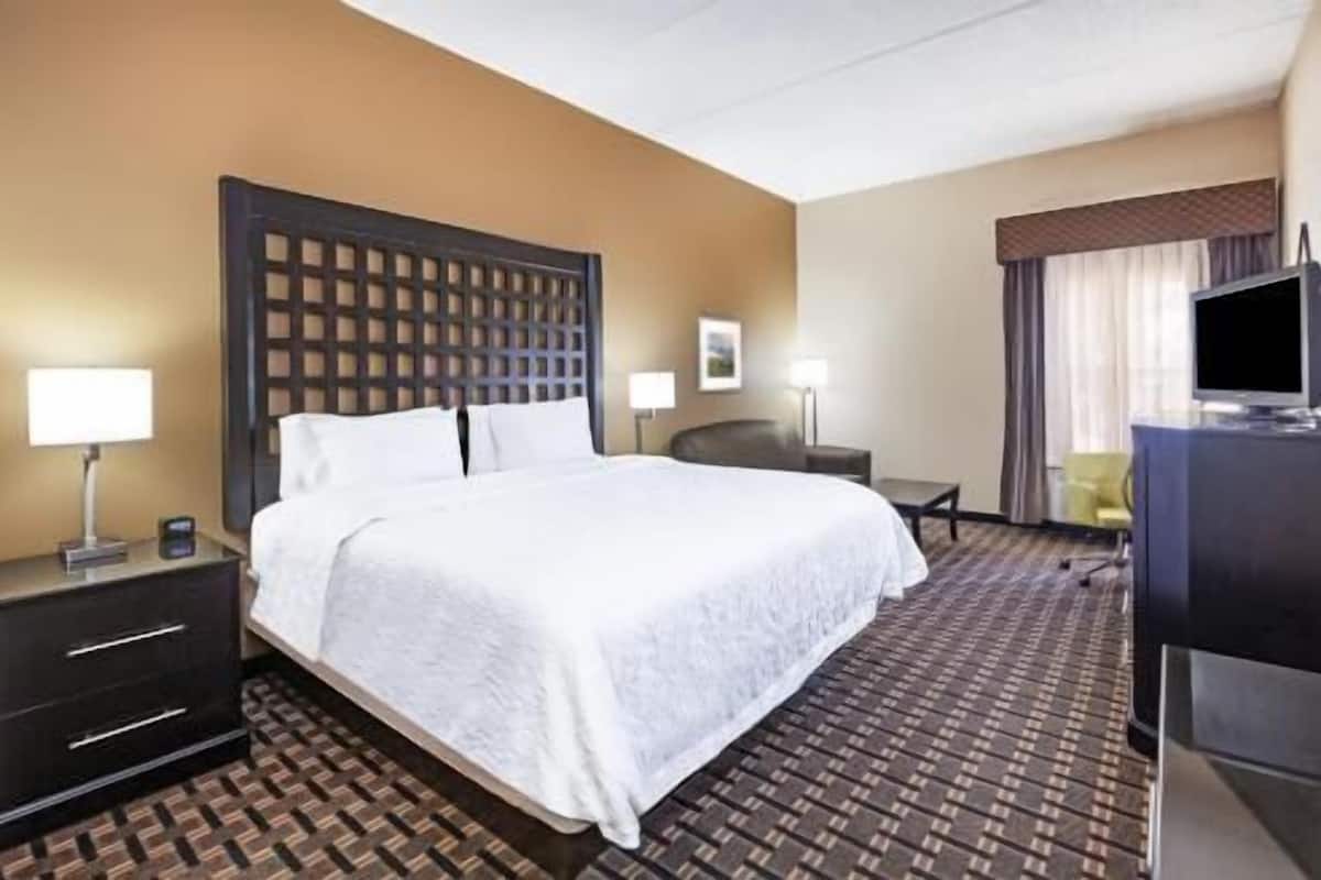 A hotel room with a large bed, a desk, a chair, a TV, and a window with curtains.