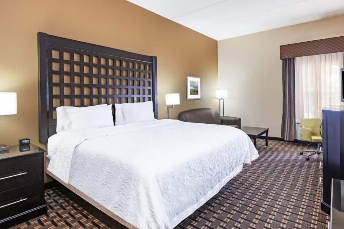 A hotel room with a large bed, a desk, a chair, a TV, and a lamp.