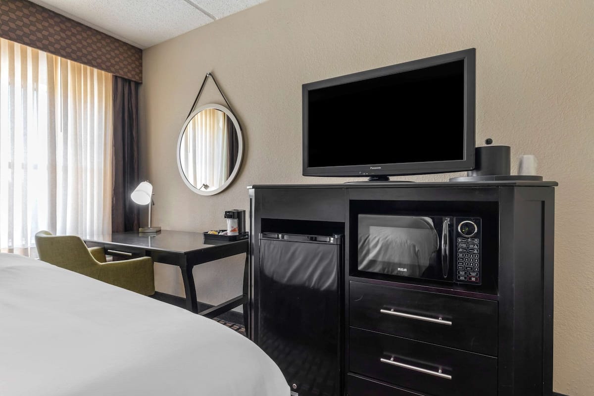 A hotel room with a bed, a desk with a chair, a television, a microwave, and a minibar.